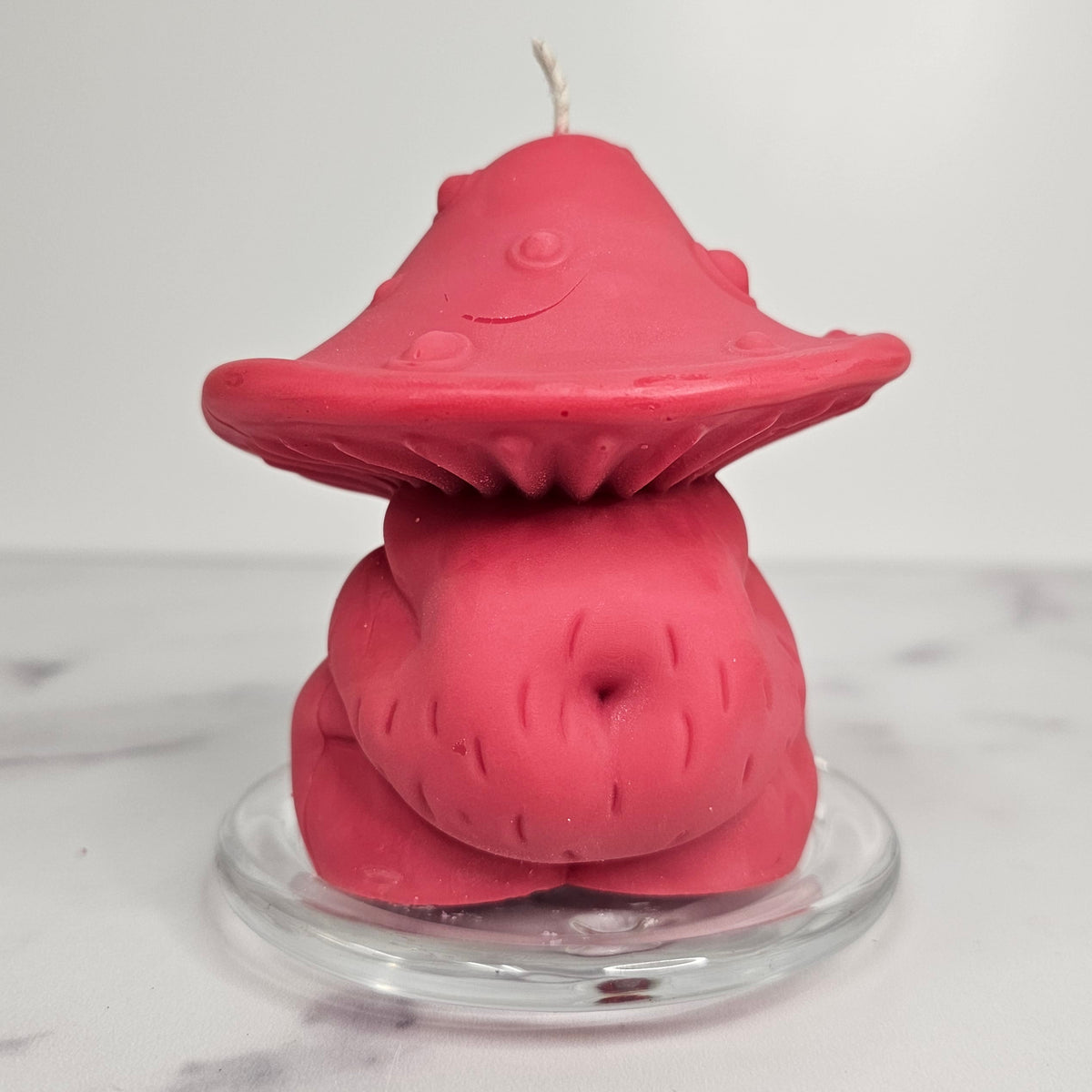 Pink mushroom-shaped body candle on a clear stand with a white background