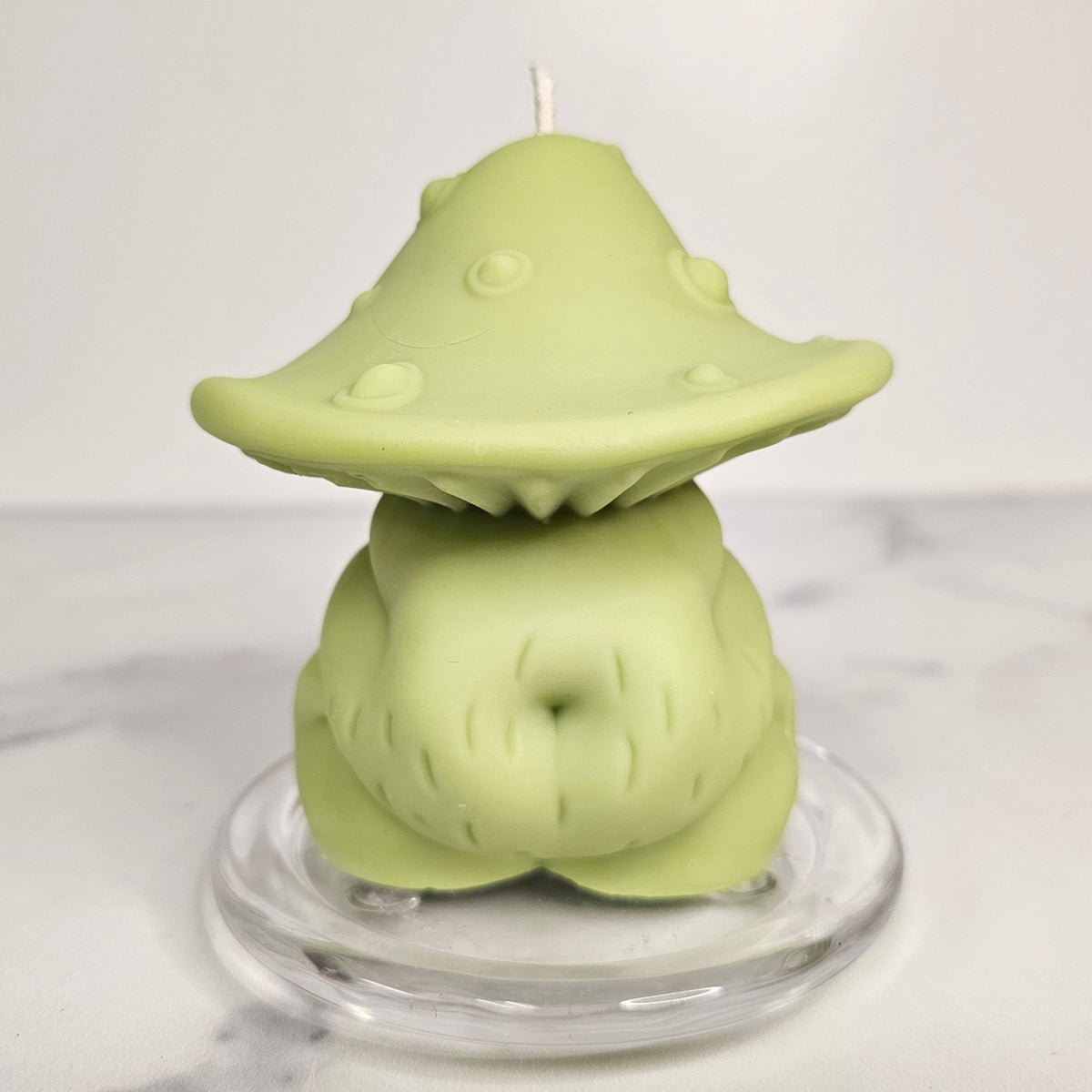 Green mushroom-shaped body candle on a clear stand with a white background